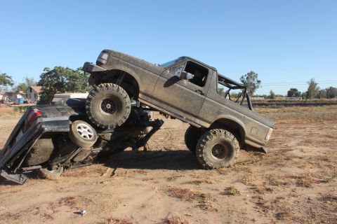 Muddy 1992 Ford Bronco on top of a crushed car, off-road