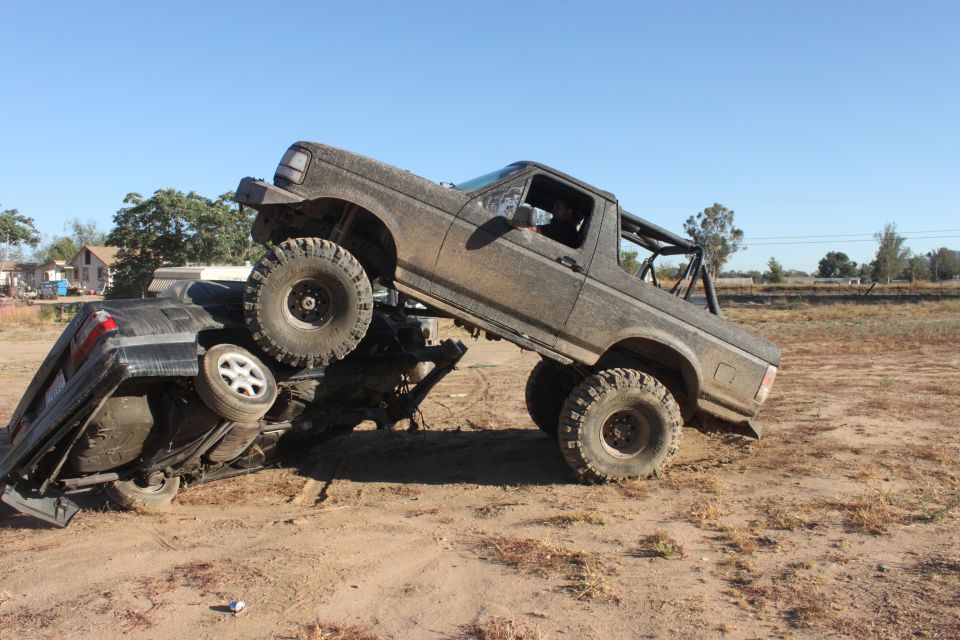 Muddy 1992 Ford Bronco on top of a crushed car, off-road