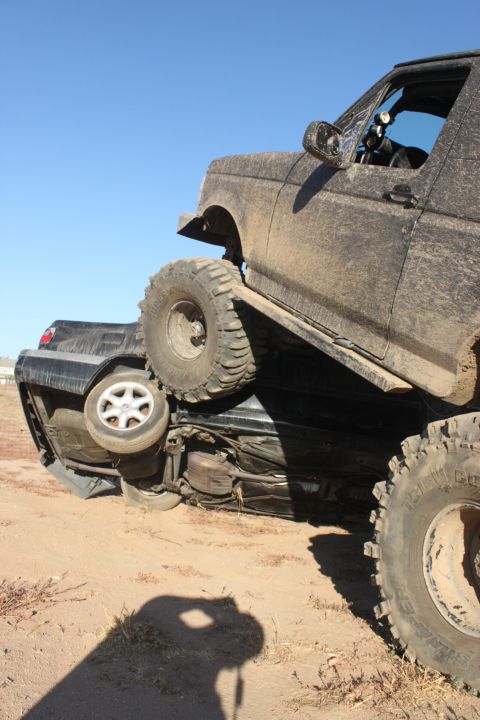 Mud-covered 1992 Ford Bronco on top of a black car, 3q-front view