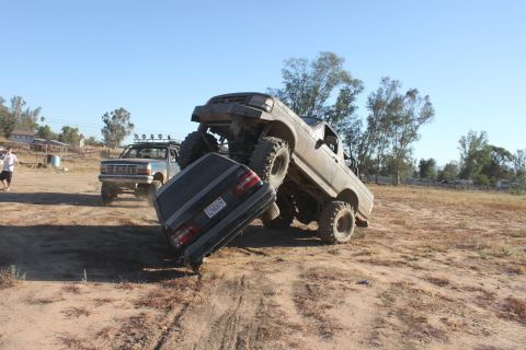 Big lifted truck on top of a car, another truck in background