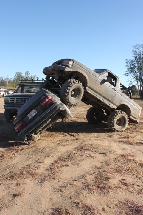 1992 Ford Bronco on top of a crushed sedan, another Bronco in background
