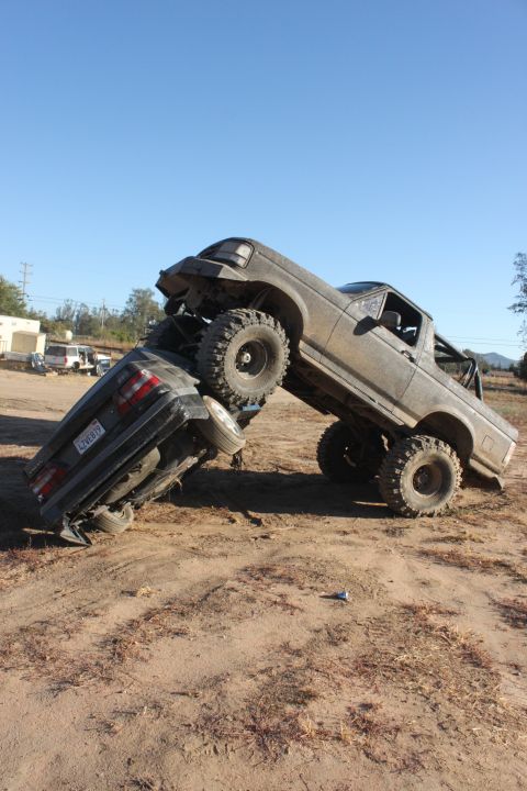 Off-road truck on top of a car in a dirt lot