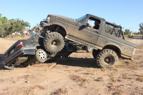 1992 Ford Bronco crushing a sedan on a dirt trail