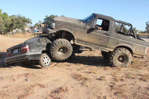 Muddy lifted truck on top of a crushed sedan
