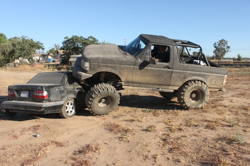 1992 Ford Bronco crushing a black sedan on a dirt road