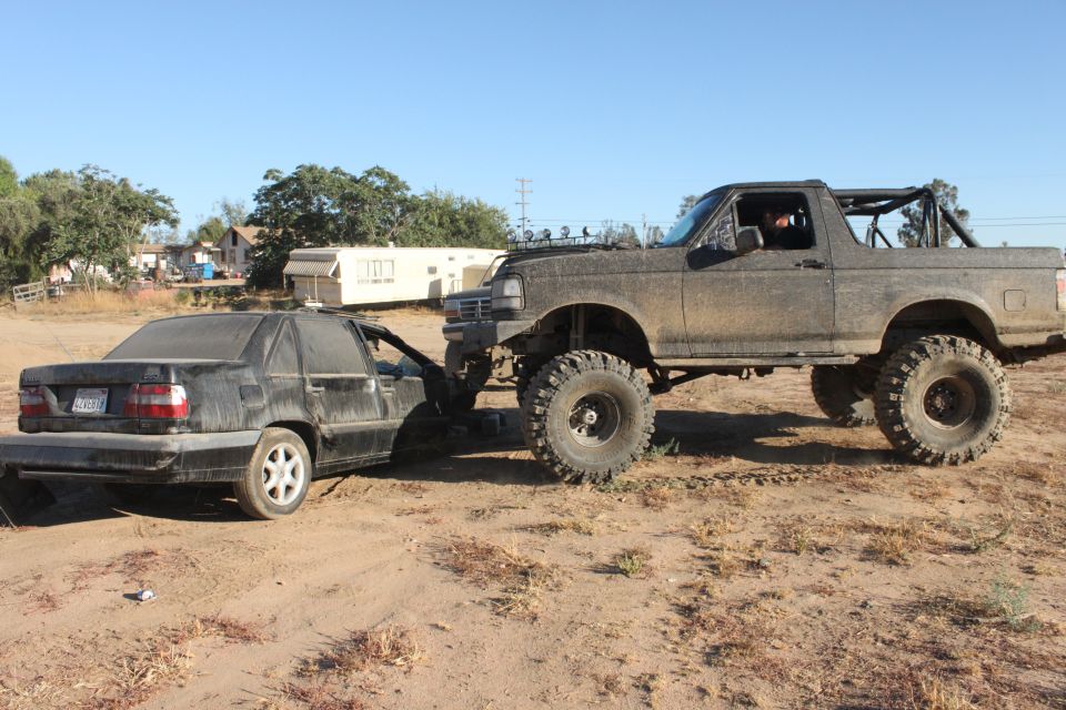 Lifted 1992 Ford Bronco towing a black sedan out of a dirt lot