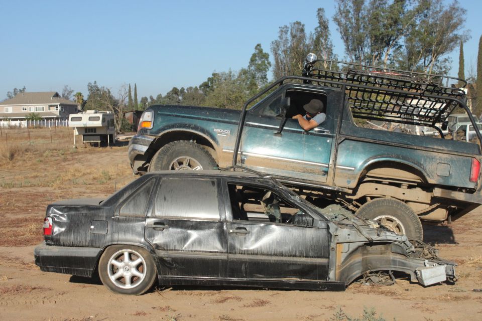 Green 1992 Ford Bronco crushing a black sedan, side view