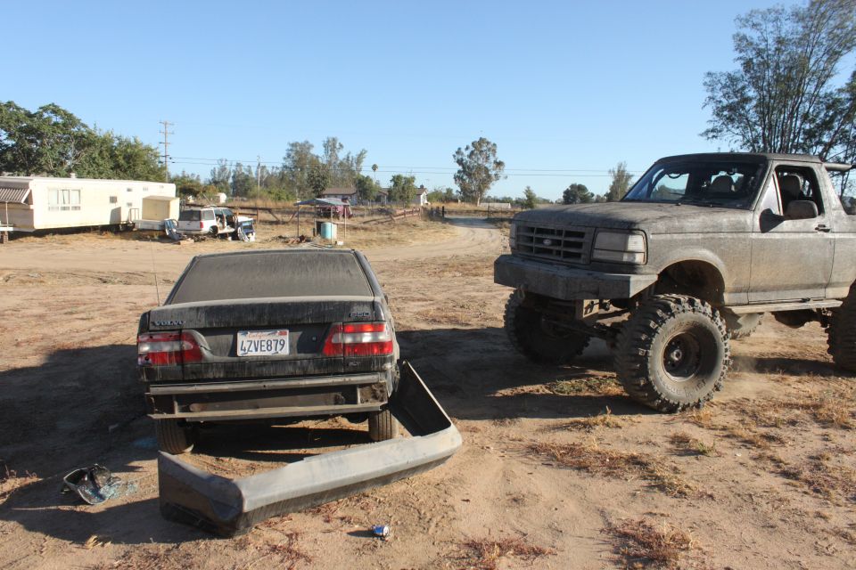 Lifted 1992 Ford Bronco with large tires, parked next to a damaged Volvo sedan