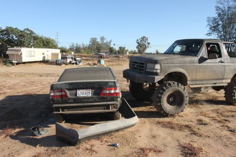 Lifted 1992 Ford Bronco parked next to a sedan with a detached bumper. License plate LZVE879 visible on sedan