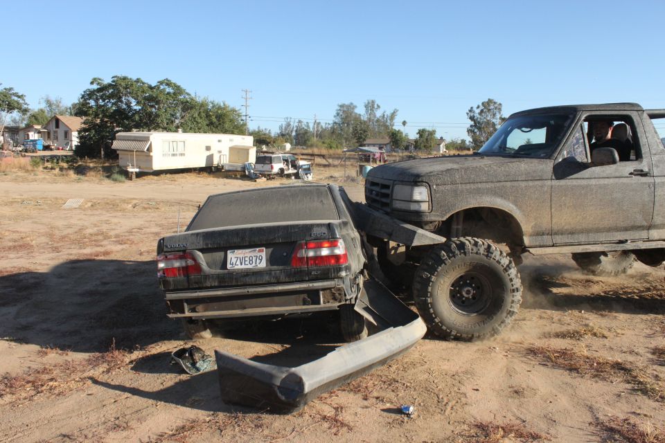 1992 Ford Bronco truck with large tires crushing a dark Volvo sedan, both covered in dust