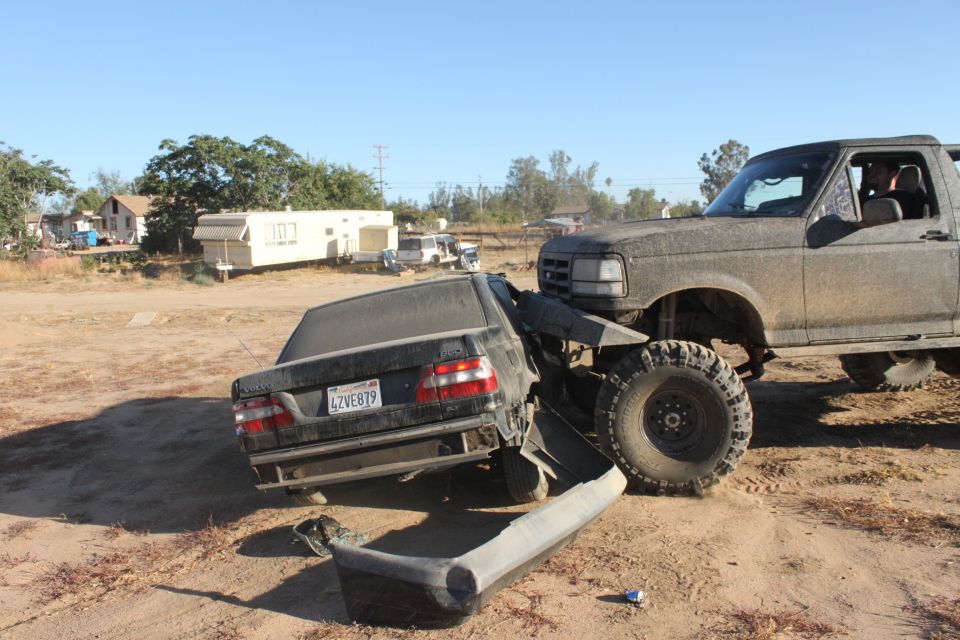 Mud-covered 1992 Ford Bronco crushing a black sedan's rear in a dirt lot