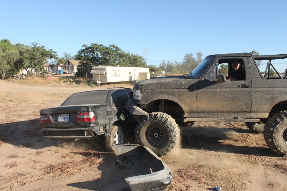 Mud-covered 1992 Ford Bronco crushing a black sedan, front bumper detached
