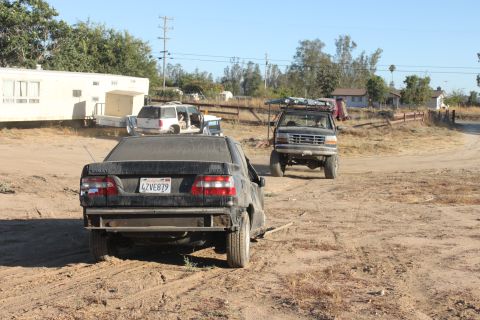 Black sedan with license plate 4ZVE879 and a lifted truck with a roof rack in a dirt lot