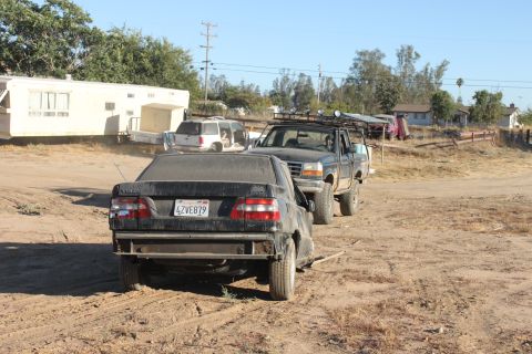 Black sedan with license plate 4ZVE879 being towed by a pickup truck with a roof rack. Trailer and SUV in back