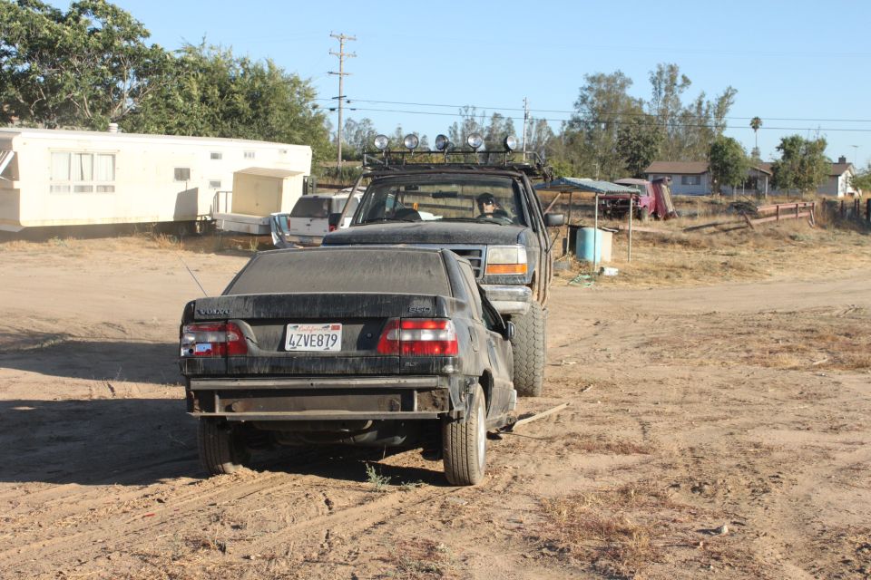 Truck towing a black sedan. Truck has lights on roof. Sedan has license plate 4ZVE879