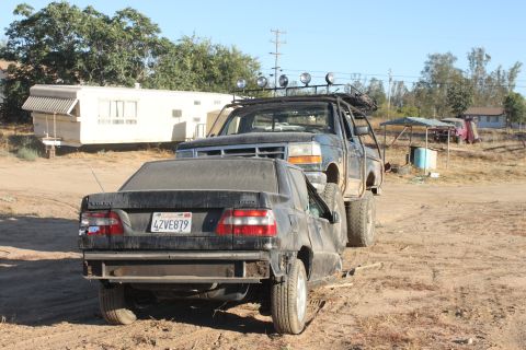 1992 Ford F-Series truck carrying a black Volvo sedan on its back, seen from the rear. License plate 4ZVE879