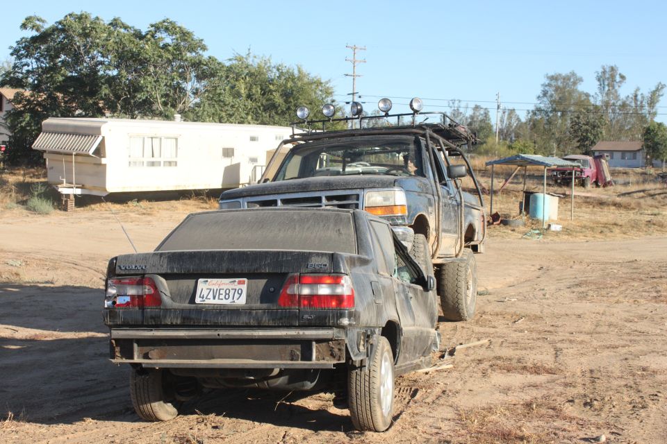 Ford pickup truck on top of a crushed Volvo sedan, with a trailer in the background