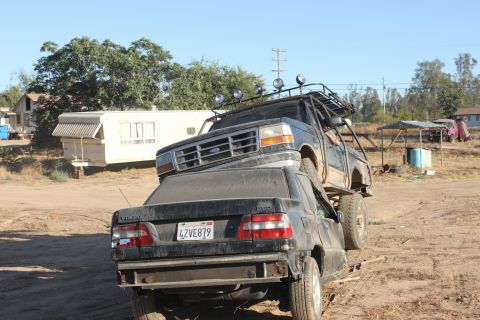 Black 1992 Ford Bronco with a roll cage and roof rack on top of a black Volvo sedan