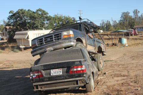 1992 Ford Bronco on top of a black Volvo sedan, both vehicles dirty, in a rural setting