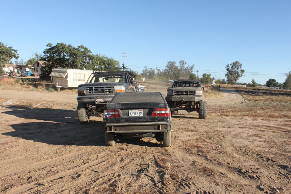 1992 Ford Bronco front view, lifted with off-road tires, parked behind a black sedan
