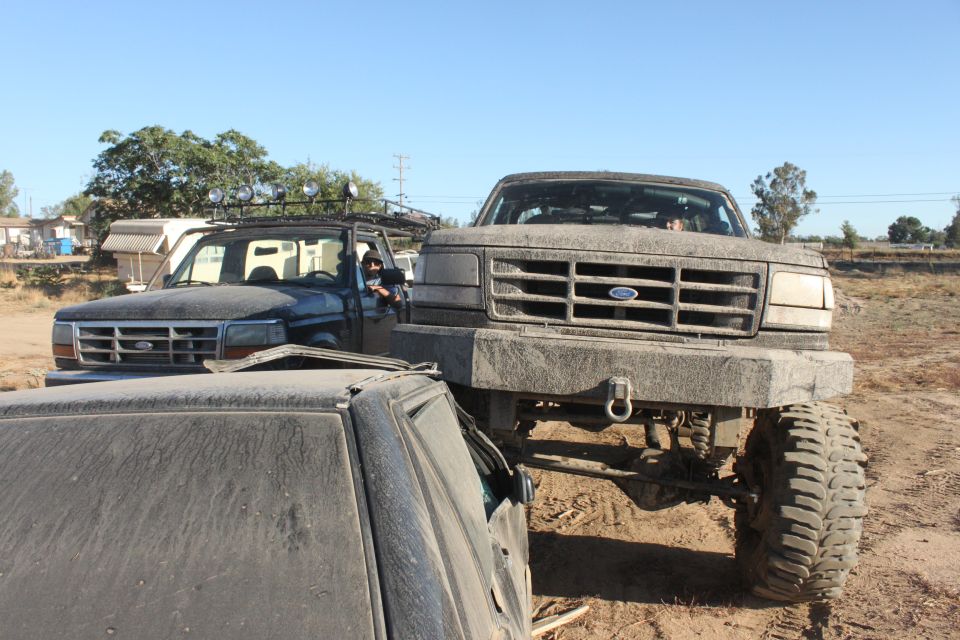 Front view of a lifted 1992-1996 Ford F-Series truck with a custom bumper, parked next to another Ford truck and a damaged car