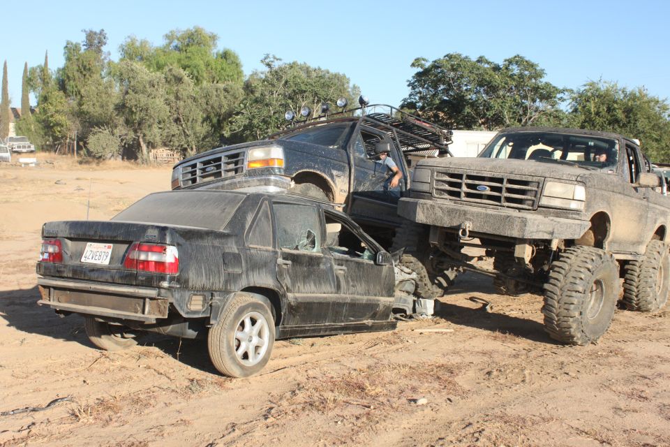Three dirt-covered vehicles are crashed together in a dry, outdoor lot