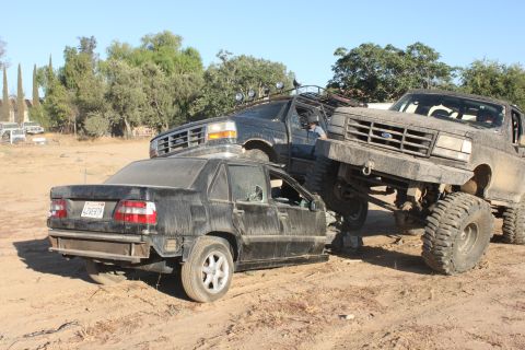Three lifted trucks crush a sedan in a junkyard