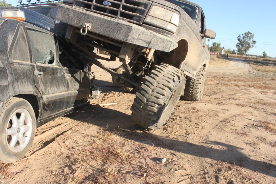 1992 Ford Bronco front end crushing a black car, lifted suspension, off-road tires