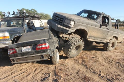 1992 Ford Bronco on top of a black Volvo sedan, both vehicles covered in dust