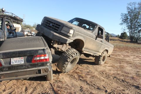 Lifted truck on top of a sedan, off-road terrain. License plate 4ZVE879