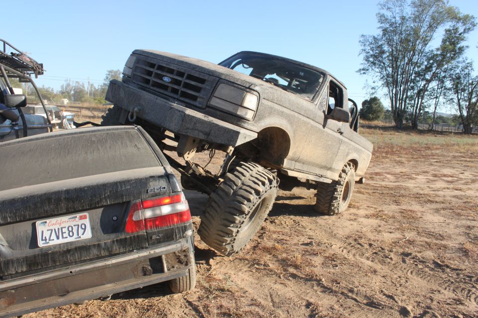 Mud-covered 1992 Ford Bronco on a dirt trail, front grille visible, with a black sedan underneath