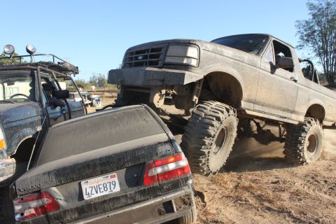 1992 Ford Bronco with large tires crushing a Volvo sedan, another vehicle visible to the left