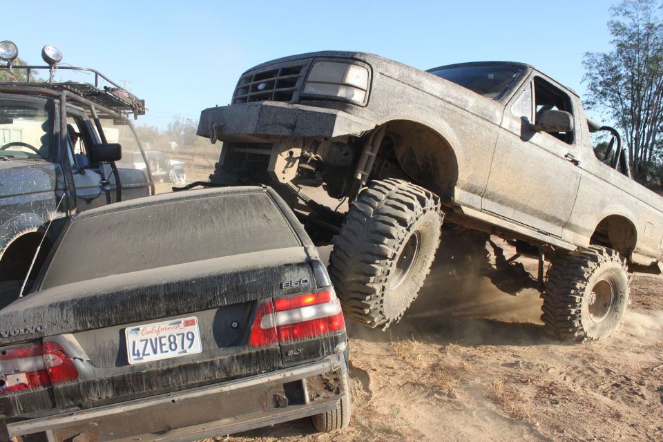 Gray 1992 Ford Bronco lifted high, front tire on a black Volvo sedan