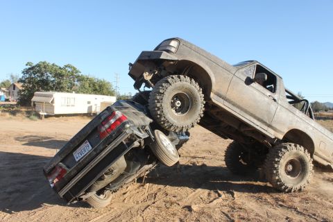 1992 Ford Bronco on top of a crushed car, off-roading