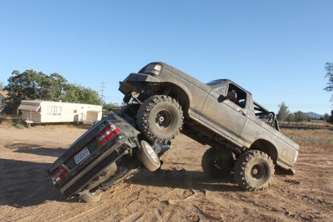 Muddy 1992 Ford Bronco crushing a sedan on a dirt trail