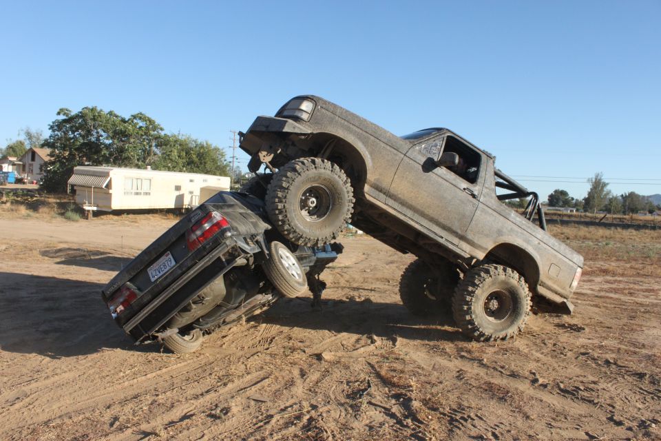 Big lifted truck on top of a car in a dirt lot