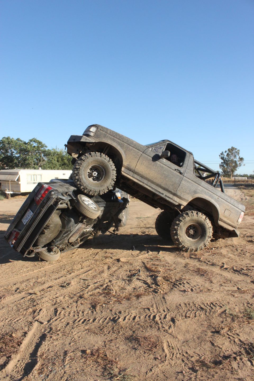 1992 Ford Bronco on top of another vehicle in a muddy off-road scene