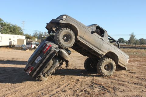 Big lifted truck on top of a car, off-roading in a dirt lot