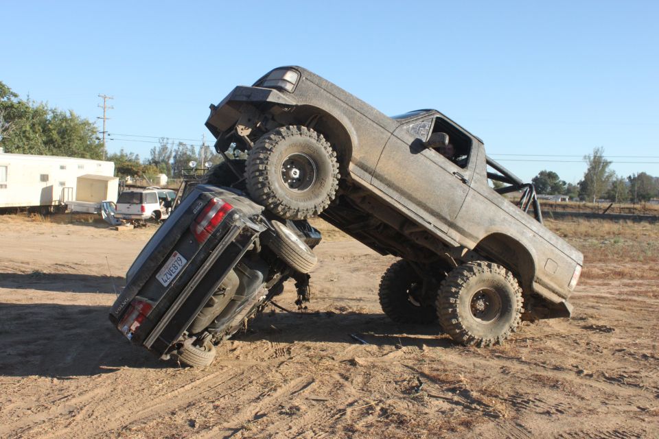 Big lifted truck on top of a car, off-roading in a dirt lot