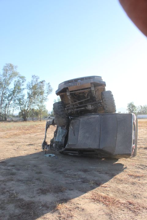 Overturned SUV lying on its side in a dirt lot with trees in the background