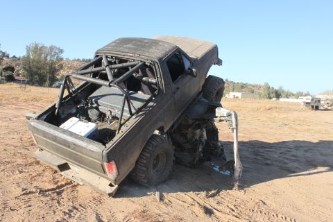 Dark grey off-road truck with roll cage, stuck on its side