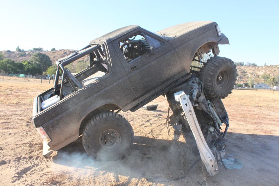 Off-road truck stuck on top of another wrecked vehicle, kicking up dust