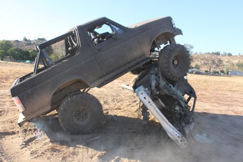 Dark gray 1992 Ford Bronco on its side, crushing a car underneath it