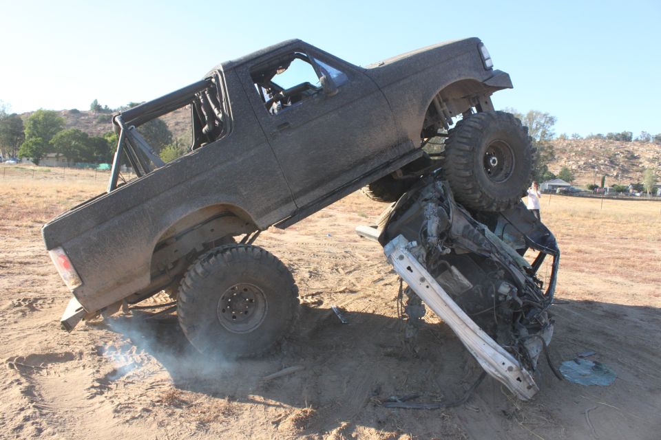 Black 1992 Ford Bronco crushing a car, lifted suspension, off-road tires