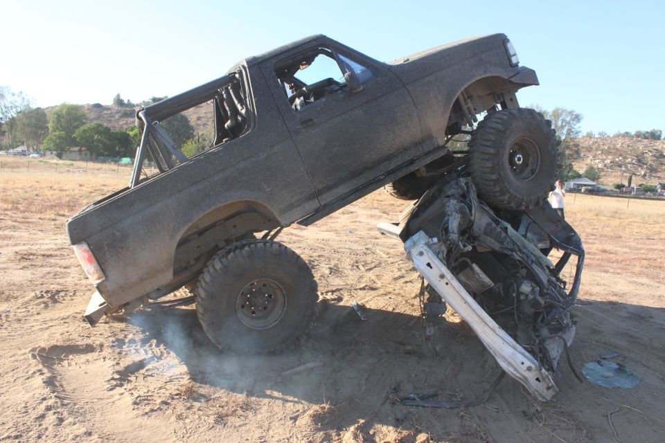 1992 Ford Bronco on top of a crushed vehicle in a dirt lot