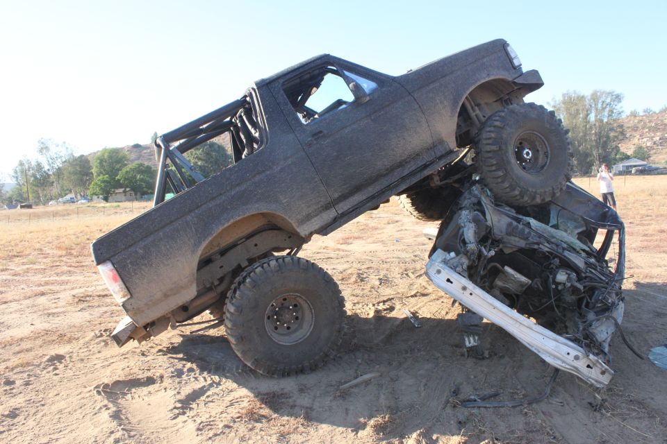 Black off-road truck on top of a crushed car, on a dirt hill