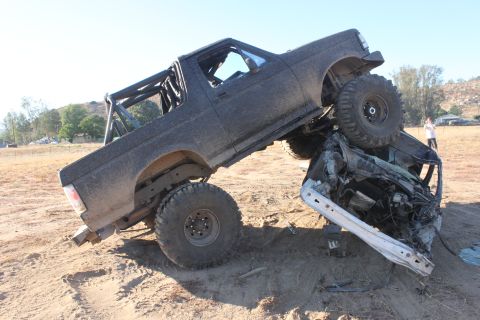 1992 Ford Bronco, dark, lifted, with roll cage, on top of a crushed car