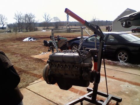1990 Ford Bronco - Engine hoist with an engine suspended, two cars visible in the background.