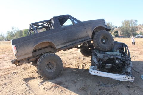 Modified 1992 Ford Bronco on top of a crushed car in a dirt lot