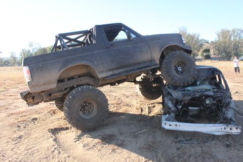 1992 Ford Bronco with roll cage on top of a crushed car, off-road tires